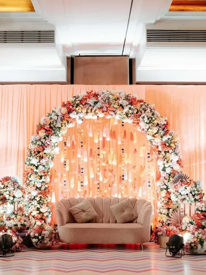 A beautiful pastel Haldi decor setup. The focal point is a floral arch in soft peach tones, creating an elegant and dreamy photo corner for the couple and their guests.