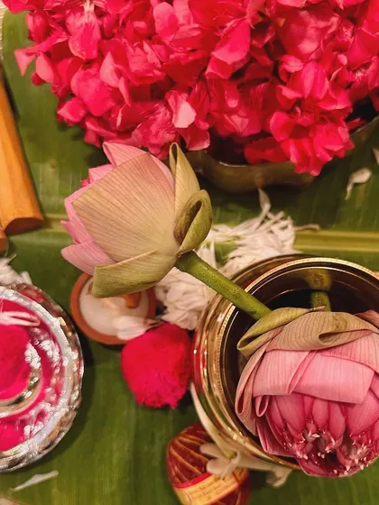 A close up of lotus buds and vibrant pink flowers in a brass vessel, placed on a banana leaf. This image captures the fresh, sacred elements used in our traditional decor.