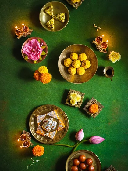 A beautiful arrangement of Diwali sweets and diyas on a rich green background. This festive flatlay highlights traditional treats like kaju katli and ladoos, creating an image of abundance and celebration for the festival of lights.
