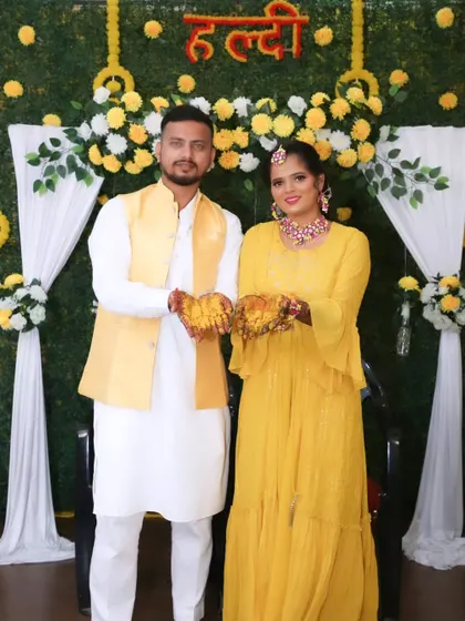 A happy couple posing at their Haldi ceremony, both dressed in coordinated yellow outfits.
