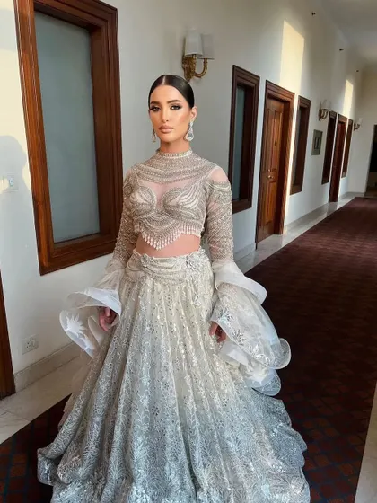 A stunning silver and white lehenga styled for a modern, angelic bride. The dramatic ruffled sleeves and intricate beadwork of this ensemble create a high-fashion statement, perfect for a grand reception.