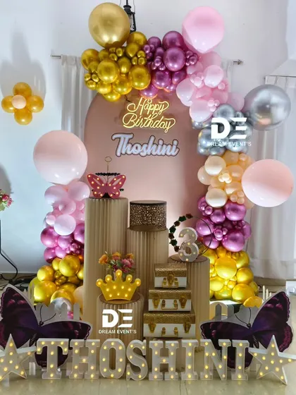 A glamorous butterfly-themed party in pink and gold, with a circular backdrop, a neon sign, and large butterfly cutouts at the base.