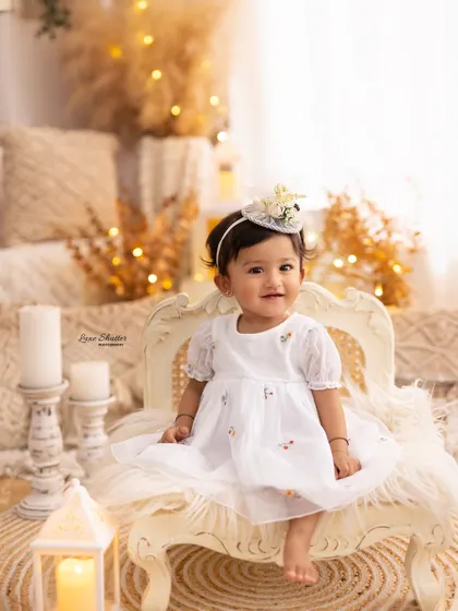 A classic portrait of the birthday girl sitting elegantly on a vintage-style chair, part of the beautiful boho first birthday setup.