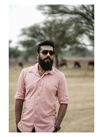 A strong outdoor portrait of a man with a beard. The natural, rural background and his confident stance create a rugged and authentic feel.