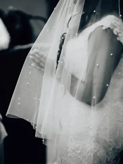 An artistic black and white detail shot of the bride through her pearl-studded veil during the ceremony. This focuses on texture and emotion.