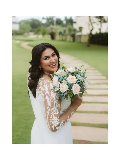 A radiant bride in a lace-sleeved gown, holding her bouquet and smiling warmly. This portrait captures her natural beauty and joyful spirit on her wedding day.