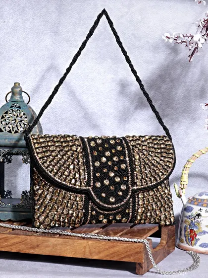 This image showcases a black and gold beaded clutch in a setting with traditional props like a lantern and kettle. The styling creates a rich, ethnic, and luxurious vibe.