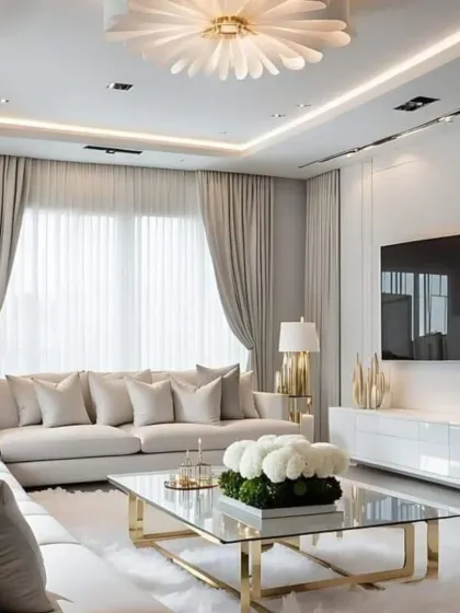 An elegant living room featuring a plush off-white sectional, a glass and gold coffee table, and a statement floral-inspired ceiling light. We used heavy, luxurious curtains and soft rugs to add texture and warmth, creating a space that is both stylish and comfortable.
