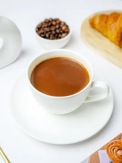 A cup of coffee styled with a croissant and coffee beans in a sophisticated, minimalist setting.