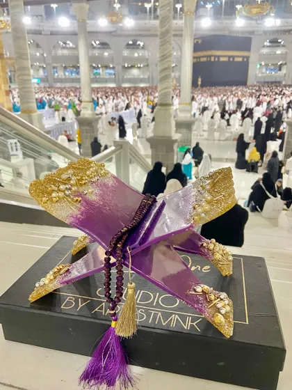 This striking Quran holder is made with a vibrant purple and gold resin design. It comes with a matching crystal tasbeeh and is shown here at the holy city of Makkah, adding to its spiritual significance.