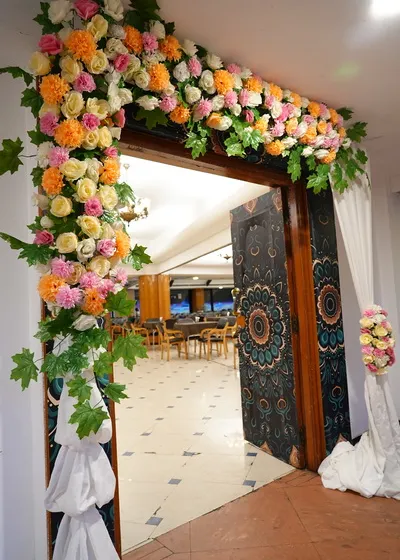 A floral arch designed to frame a doorway, decorated with pastel-colored roses and carnations. This is a simple way to make an entrance feel special.