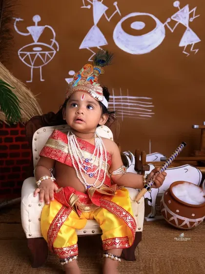 A regal pose from our little Krishna. Seated on a miniature throne, he holds a flute, looking every bit the part in this beautifully styled Janmashtami photoshoot.