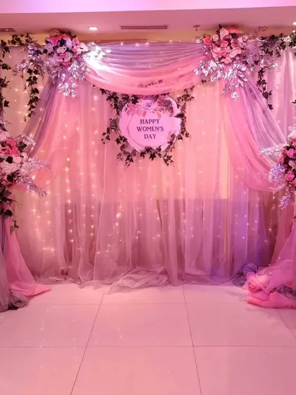 I design elegant backdrops for special occasions like Women's Day. This setup features soft pink draping, twinkling fairy lights, and beautiful floral arrangements, creating a sophisticated and celebratory atmosphere.