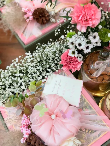 The delicate details of our Roka favors. A fabric-wrapped gift box is topped with a handmade floral arrangement, pinecones, and whimsical butterflies, accompanied by a handwritten note.