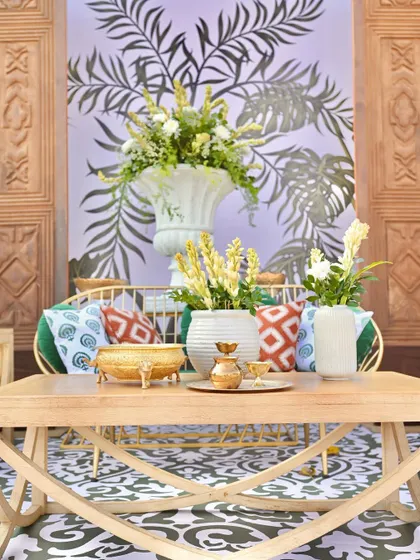 A close-up of a lounge area with a beautiful hand-carved wooden backdrop, a comfortable sofa with printed cushions, and elegant floral arrangements.