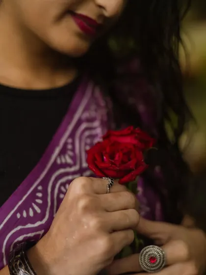 A detail-oriented shot focusing on the hands holding red roses. This image highlights the model's jewelry and the rich color of her saree, telling a story through small, beautiful details.