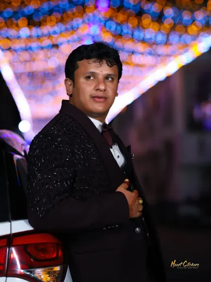 A candid portrait of the groom leaning against a car, with colorful bokeh lights in the background.