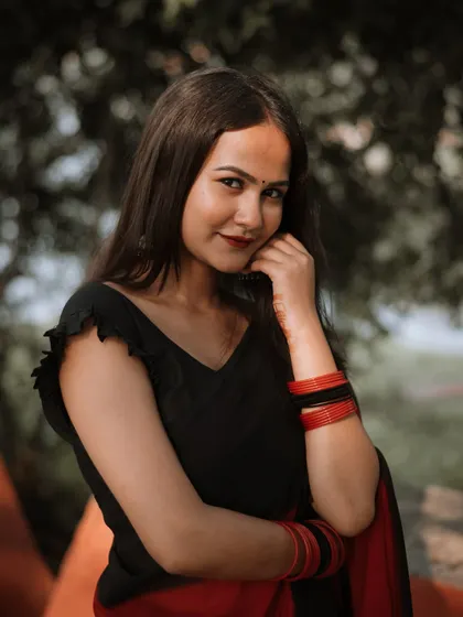 A gentle smile and a classic pose make this portrait special. The focus is on the model's natural expression, complemented by the traditional red and black saree and matching bangles.