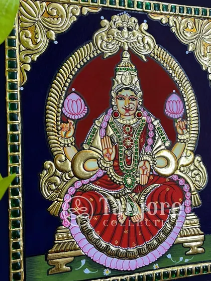 Goddess Lakshmi, sitting on a lotus, smiling upon us and blessing us all with her glory. This finished painting showcases the classic elements of Tanjore art, from the green Kundan stone border to the intricate gold work.