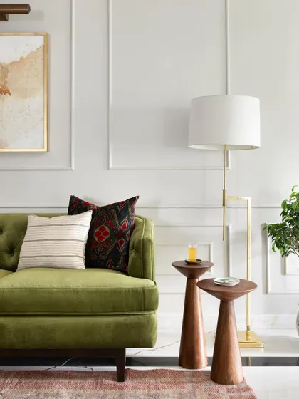 A detail from the living room of the Madras Home. The olive green tufted sofa is paired with modern wooden nesting tables and a brass floor lamp.