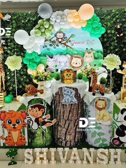 A vibrant jungle party for Shivansh's 5th birthday. This decor features a backdrop of green foliage, cute animal characters, and tree-stump-themed pedestals, bringing the excitement of the wild indoors.