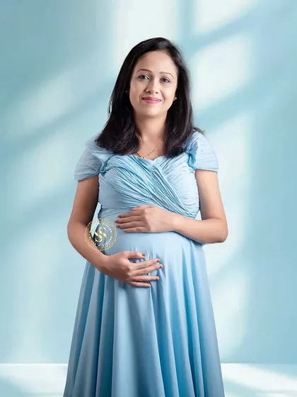 A simple and elegant solo maternity portrait against a soft blue studio backdrop. The lighting creates a beautiful, gentle effect.