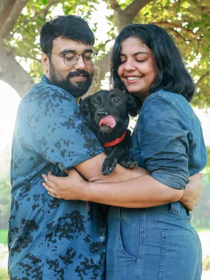 A warm embrace with a furry family member. This outdoor couple's portrait shows the pure love and happiness that pets bring into our lives. Look at that happy tongue lick!