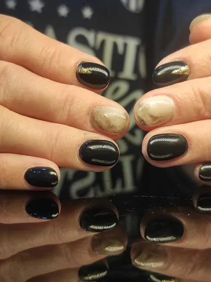 A chic black manicure with marbled accent nails featuring a touch of gold.