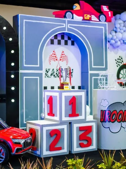 The main stage for the race car party, complete with a mini ride-on car, winner's podium blocks, and a custom backdrop. It's the perfect setup for a future champion.