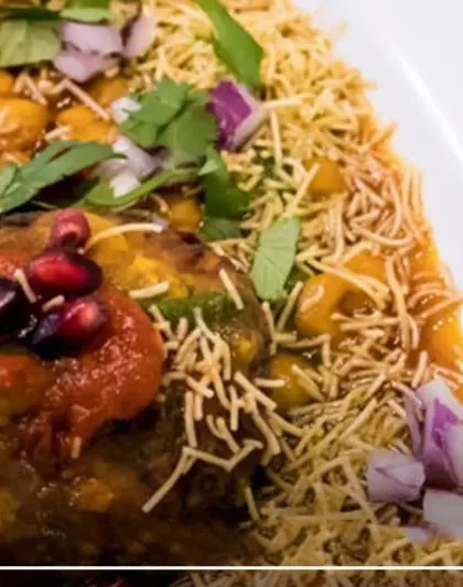 A close-up of our expertly prepared Aloo Tikki Chaat. It's a perfect blend of textures and flavors, with a crispy potato patty, savory chutneys, cool yogurt, and a garnish of fresh pomegranate.