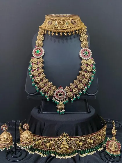 This bridal set features a unique floral haaram paired with a traditional temple choker. The combination of red and green stones makes it a versatile choice for many silk sarees.