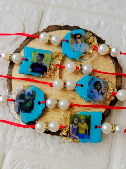 A set of five custom photo rakhis, each featuring a different picture preserved in resin with pearl accents.