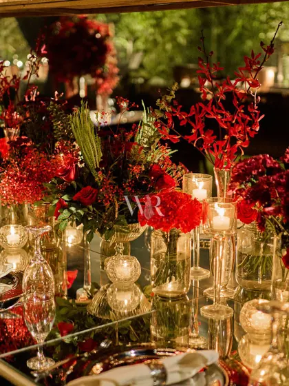 The reflection of red flowers and candlelight on a mirrored tabletop. This detail shot captures the glamour and romance of the tablescape design.