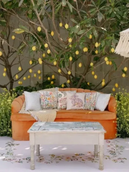 A cozy seating area under a lemon tree, with a vibrant orange sofa and custom cushions. We create these little nooks for guests to discover and enjoy.