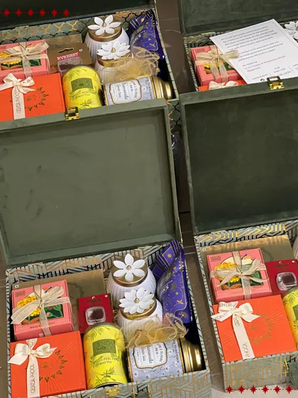 An inside look at the green velvet Diwali hampers being prepared for a bulk order. They are filled with colorful boxes of tea, sweets, and decorative jars.