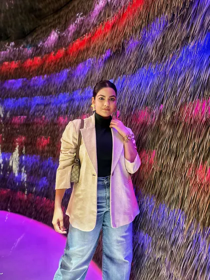 A classic combination of a beige blazer, black turtleneck, and blue jeans, taken to the next level by a colorful, artistic background.