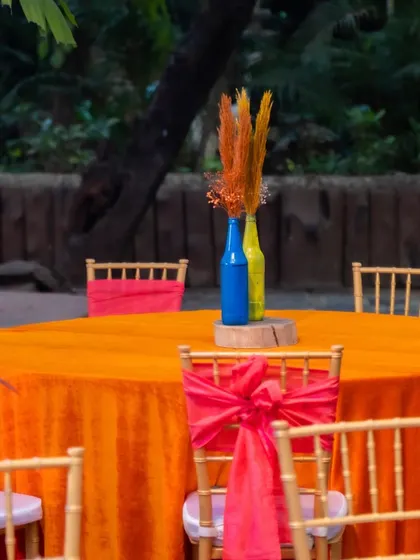 A close-up of a guest table with a bright orange tablecloth and chairs with red sashes, showing the bold color choices for the carnival theme.