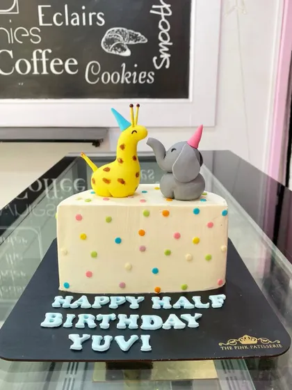 A cute and simple half-birthday cake. The design features colorful polka dots and is topped with a tiny fondant giraffe and elephant wearing party hats.