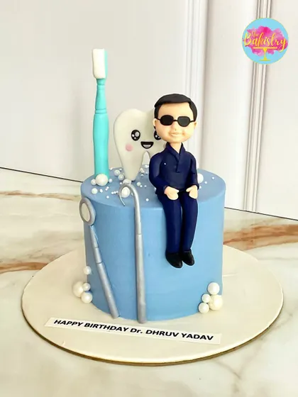 A unique and adorable cake for Dr. Dhruv Yadav, featuring a dentist figurine, a toothbrush, and a smiling tooth. Perfect for a dental professional’s birthday!