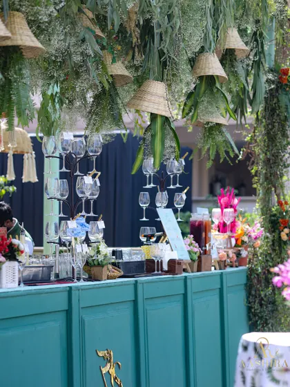 A closer look at the botanical bar, showing the hanging glass racks and the lush greenery canopy with woven lampshades.