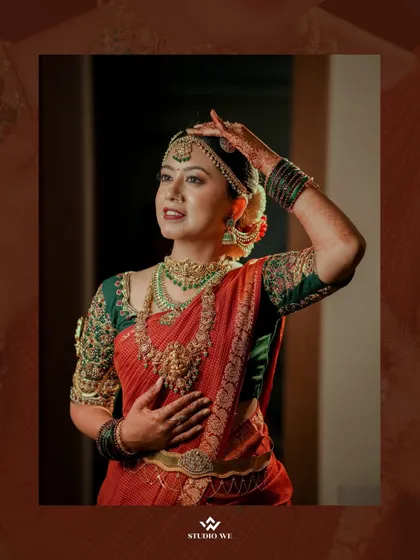 A beautiful portrait of the bride in her red wedding saree, her hand gracefully touching her elaborate jewelry.