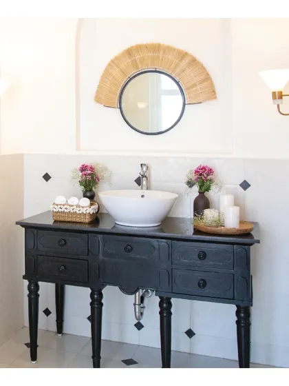 The son's bathroom in this holiday villa is a playful combination of black and white tiles. We designed a custom walnut vanity counter and paired it with a quirky cane mirror to create a space that is both youthful and stylish.