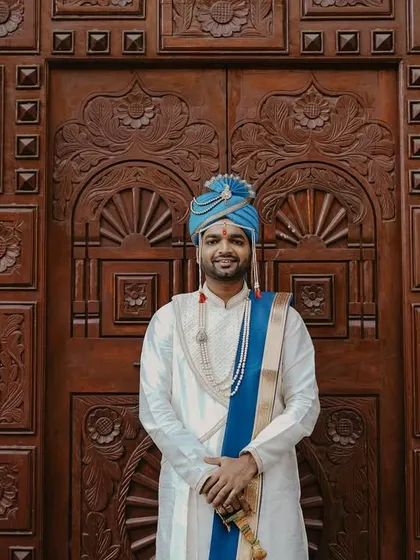 A confident and happy portrait of the groom in his traditional wedding attire, standing before an ornate wooden door.