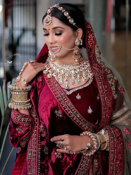 A classic bridal portrait focusing on the intricate details of the jewellery. The bride's pose draws attention to her layered necklaces and the fine embroidery on her velvet blouse.
