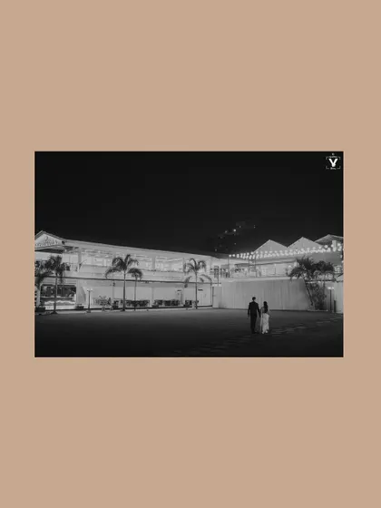 A minimalist black and white shot of a couple walking across a lawn at night. The vast empty space and the distant building create a cinematic and slightly mysterious feel.