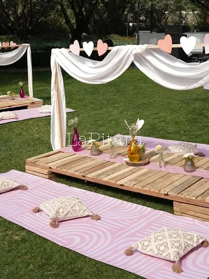 A cozy low-seating arrangement at a Valentine's picnic, with wooden pallets as tables and comfortable cushions on the grass.