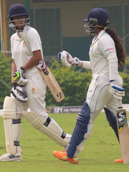 Two batters walk between the wickets, a moment of partnership during an innings.