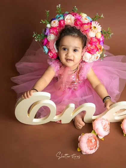 This little girl in a pink dress and a stunning floral bonnet is celebrating her first birthday.