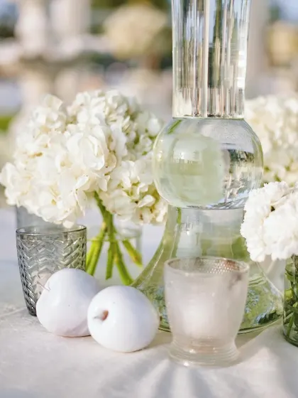 A close-up of the table decor, featuring white apples and textured glass candle holders alongside a crystal vase. The mix of materials adds interest and sophistication.
