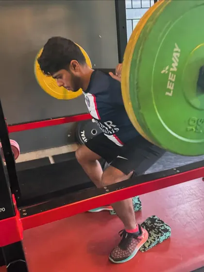 A young athlete performs a barbell squat with elevated heels to improve his form and depth, showing our attention to detail for clients of all ages.